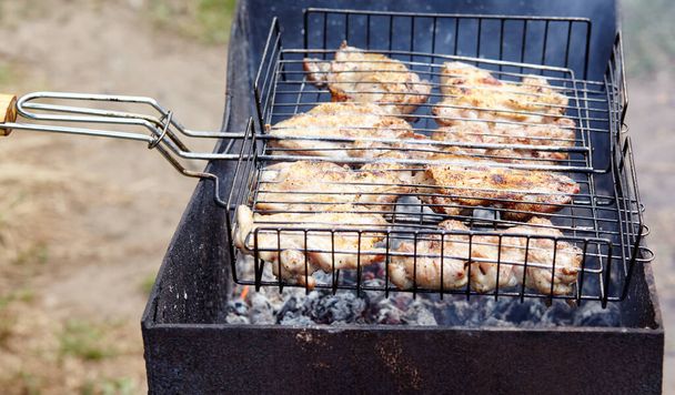 Tasty chicken wings cooking on barbecue grill, outdoors. Roasted chicken meat, closeup - Φωτογραφία, εικόνα