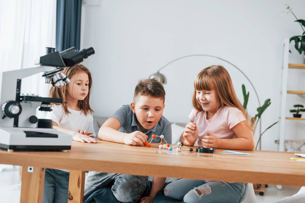 Using microscope. Kids having fun in the domestic room at daytime together. - Φωτογραφία, εικόνα