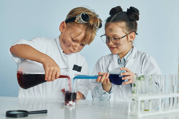 Little girl and boy in white coats plays a scientists in lab by using equipment. - Fotoğraf, Görsel