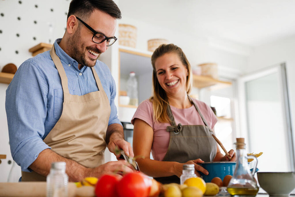 Young happy couple is enjoying and preparing healthy meal in their kitchen together. People food happiness concept. - Фото, зображення