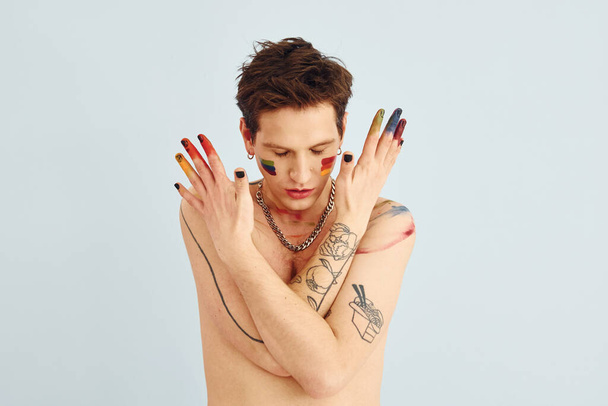 Young gay man is standing in the studio and posing for a camera. Shirtless guy with rainbow make up. - Fotoğraf, Görsel