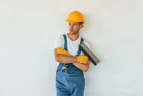 Posing for the camera. Young man working in uniform at construction at daytime. - Foto, afbeelding
