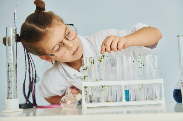 Workes with liquid that is in test tubes. Little girl in coat playing a scientist in lab by using equipment. - Zdjęcie, obraz