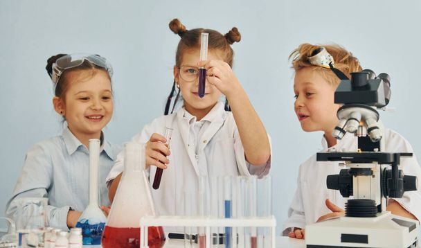 Tesztcsövek színes folyadékkal. A fehér kabátos gyerekek tudósokat játszanak a laborban felszereléssel.. - Fotó, kép