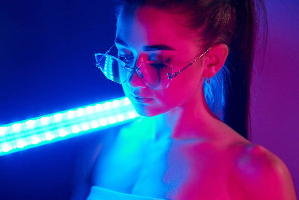 Holds neon lighting stick. Fashionable young woman standing in the studio. - Foto, Imagem
