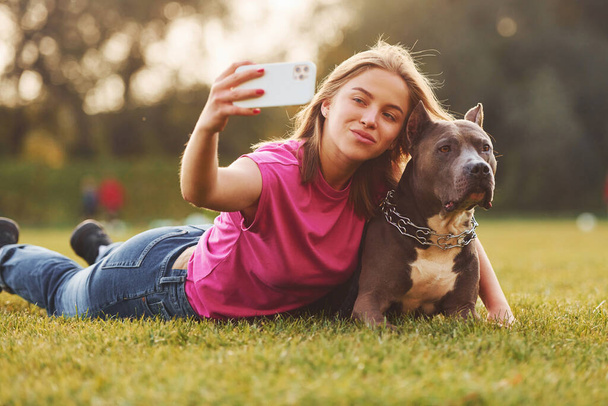 Making selfie. Woman in casual clothes is with pit bull outdoors. - Foto, Bild