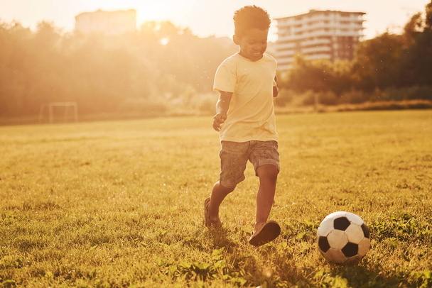 Plays soccer. African american kid have fun in the field at summer daytime. - 写真・画像