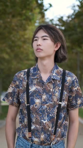 Portret młodego Tajwańczyka patrzącego w kamerę i uśmiechającego się w parku. - Materiał filmowy, wideo