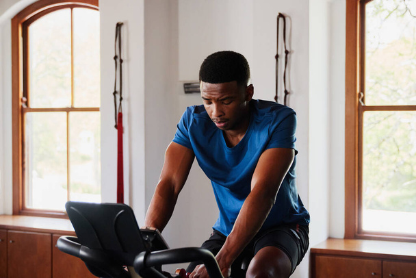 Determined young black man in sportswear doing cardio workout on exercise bike at the gym - Foto, Imagen