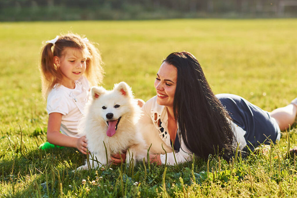 Little girl and woman laying down on the grass with their cute dog. - Fotó, kép