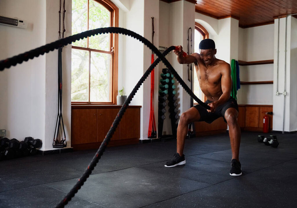 Determined young black man doing a workout with battle ropes at the gym - Foto, immagini