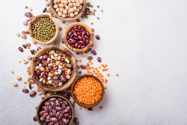 Top view of different beans, lentils, mung, chickpeas in wooden bowls for tasty meals on grey concrete background - Foto, imagen