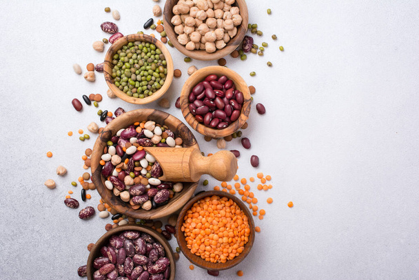 Top view of different beans, lentils, mung, chickpeas in wooden bowls for tasty meals on grey concrete background - Φωτογραφία, εικόνα