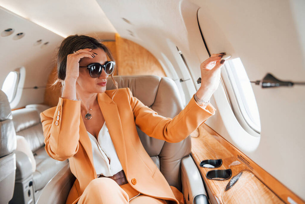 In sunglasses. Young passenger woman in yellow clothes is flying in the plane. - Foto, Imagem
