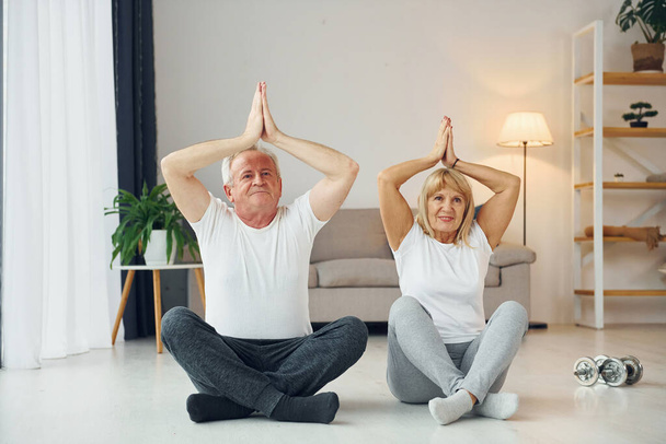 Doing yoga. Senior man and woman is together at home. - Photo, image