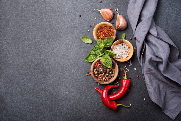 Top view of peppercorn, salt, garlic, basil and red hot chilli pepper for spicy and aromatic food on dark concrete background with copy space - Photo, image