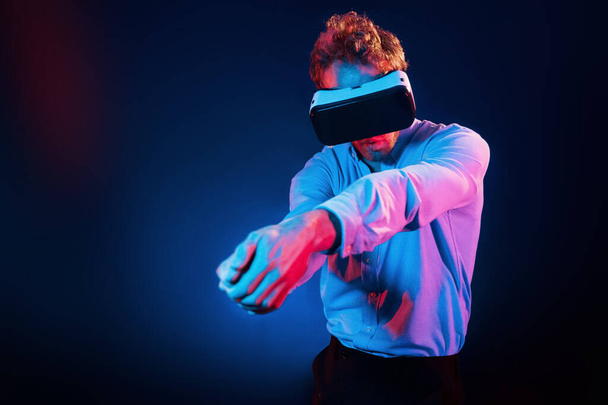 Virtual glasses gaming experience. Neon lighting. Young european man is in the dark studio. - Фото, изображение