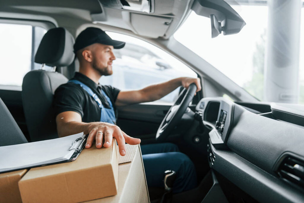 Modern vehicle. Delivery man in uniform is indoors with car and with order. - Photo, image