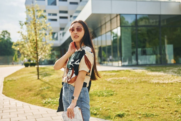 In sunglasses. Young asian woman is outdoors at daytime. - Фото, изображение