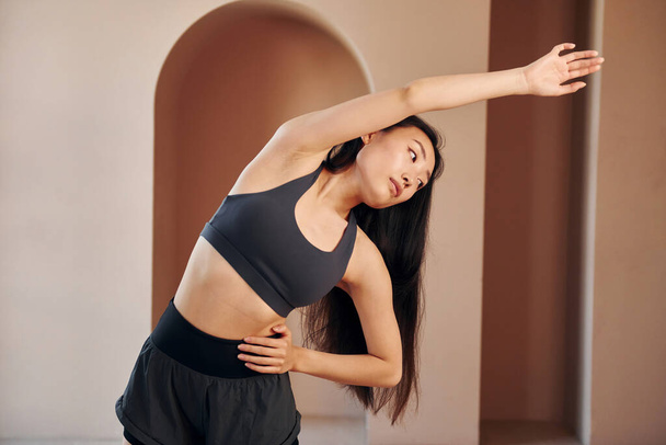 Doing fitness exercises. Young serious asian woman standing indoors. - Φωτογραφία, εικόνα