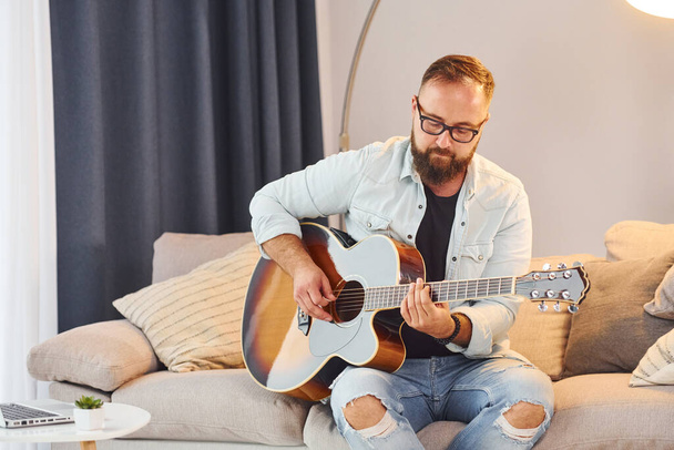 Cozy atmosphere. Man in casual clothes and with acoustic guitar is indoors. - Fotoğraf, Görsel