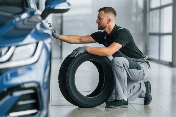 Tire on the floor. Man in uniform is working in the autosalon at daytime. - Fotoğraf, Görsel