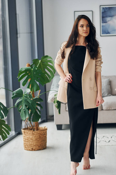In black dress and jacket. European woman in fashionable stylish clothes is posing indoors. - Foto, imagen