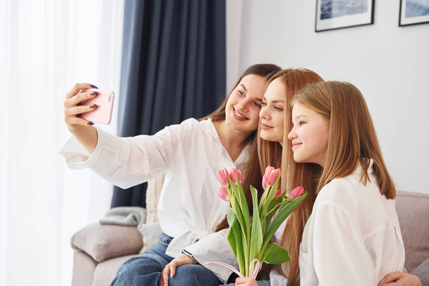 Making selfie. Young mother with her two daughters at home at daytime. - Foto, Bild