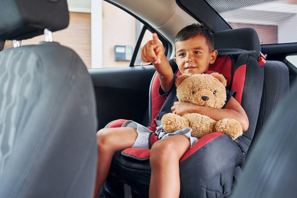 Little boy with teddy bear is sitting in the automobile. - Фото, зображення
