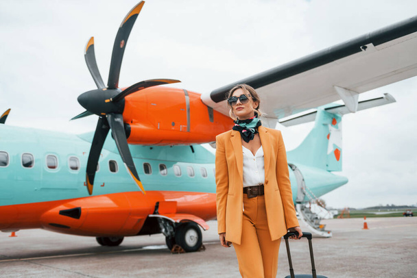 Passenger woman that is in yellow clothes, sunglasses and with luggage is outdoors near plane. - 写真・画像