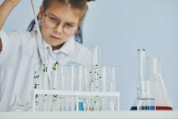 Works with test tubes. Little girl in coat playing a scientist in lab by using equipment. - Foto, Bild