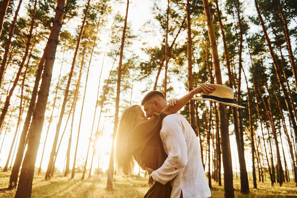 Against background with sunshine. Happy couple is outdoors in the forest at daytime. - Foto, afbeelding