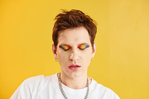 Young gay man is standing in the studio and posing for a camera. Against yellow background. - 写真・画像