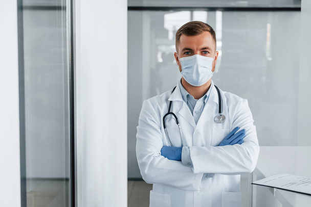 In blue gloves. Professional medic in white coat is in the clinic. - Foto, afbeelding