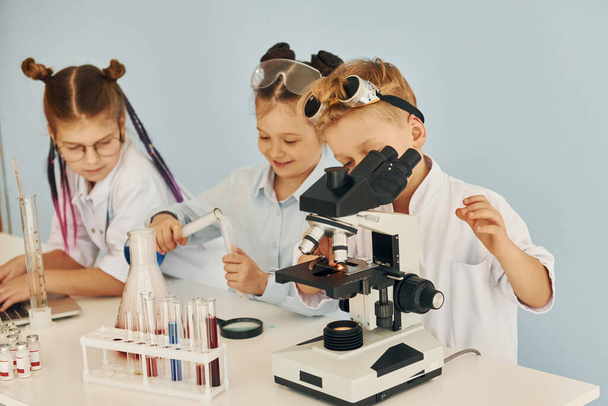 Using microscope. Children in white coats plays a scientists in lab by using equipment. - Φωτογραφία, εικόνα