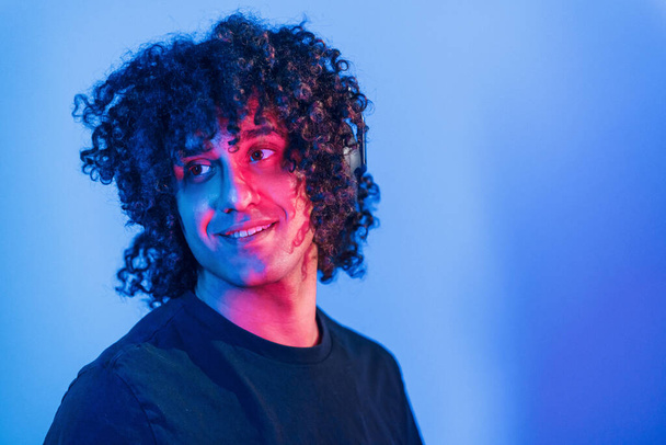 Young beautiful man with curly hair is indoors in the studio with neon lighting. - Foto, imagen