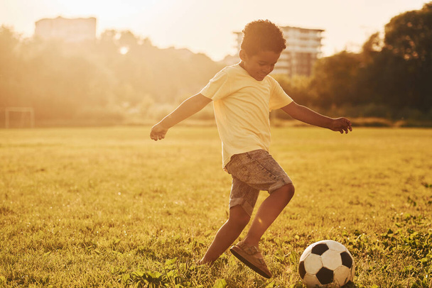 Plays soccer. African american kid have fun in the field at summer daytime. - 写真・画像