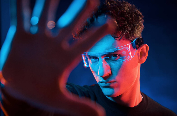 Close up portrait. Neon lighting. Young european man is in the dark studio. - Фото, изображение