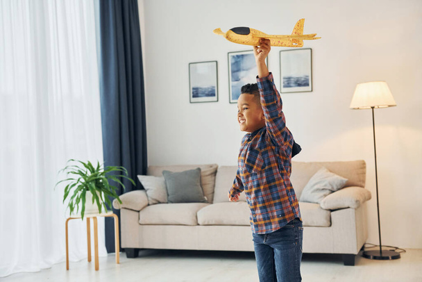 Playing with yellow toy plane. Cheerful young boy is at home alone. - Photo, image