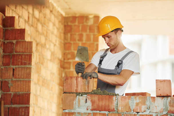 Bricks installation. Young man working in uniform at construction at daytime. - Φωτογραφία, εικόνα