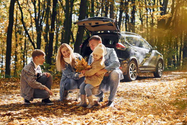 Car is behind. Happy family is in the park at autumn time together. - Foto, Imagen