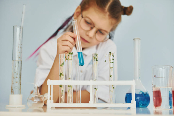 Workes with liquid that is in test tubes. Little girl in coat playing a scientist in lab by using equipment. - Φωτογραφία, εικόνα