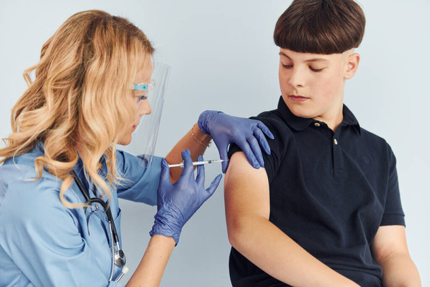 Médico en uniforme haciendo vacunación al chico con camisa negra. - Foto, imagen