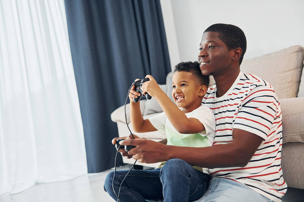 Playing video games. African american father with his young son at home. - 写真・画像