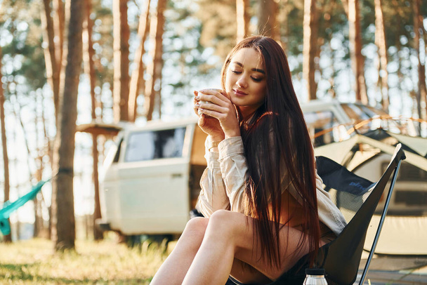 Takes a break and drinking out of cup. Woman is traveling alone in the forest at daytime. - Foto, imagen