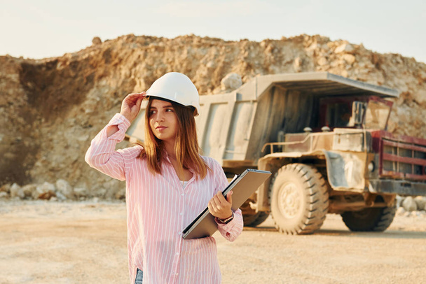 With documents. Young woman with documents in hard hat is standing on the borrow pit. - Photo, image