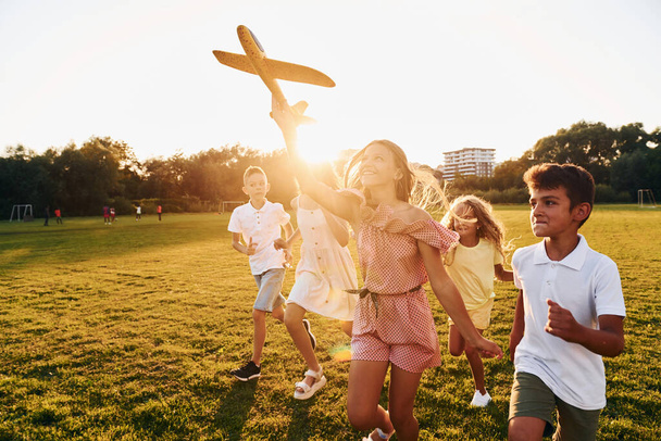 Playing with toy plane. Group of happy kids is outdoors on the sportive field at daytime. - Foto, Bild