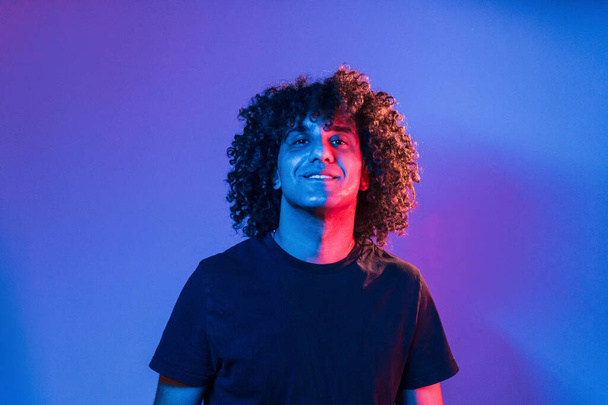 Young beautiful man with curly hair is indoors in the studio with neon lighting. - Foto, Imagem