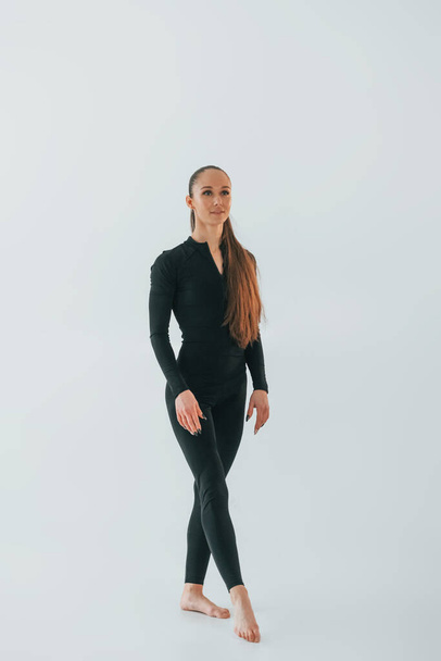 V černém sportovním oblečení. Mladá žena dělá gymnastiku uvnitř. - Fotografie, Obrázek