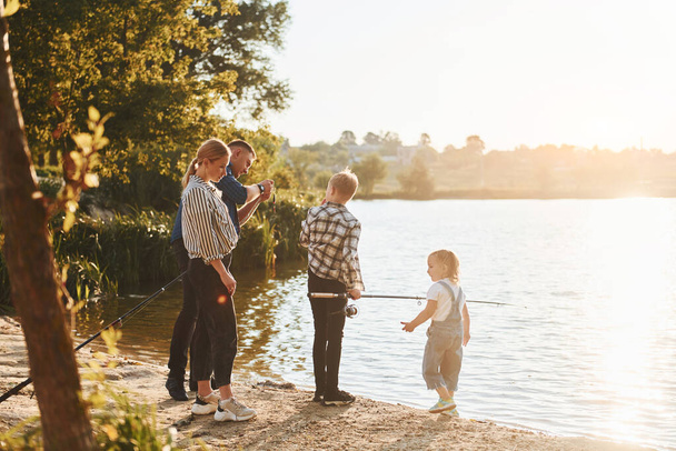 Beautiful nature. Father and mother with son and daughter on fishing together outdoors at summertime. - 写真・画像